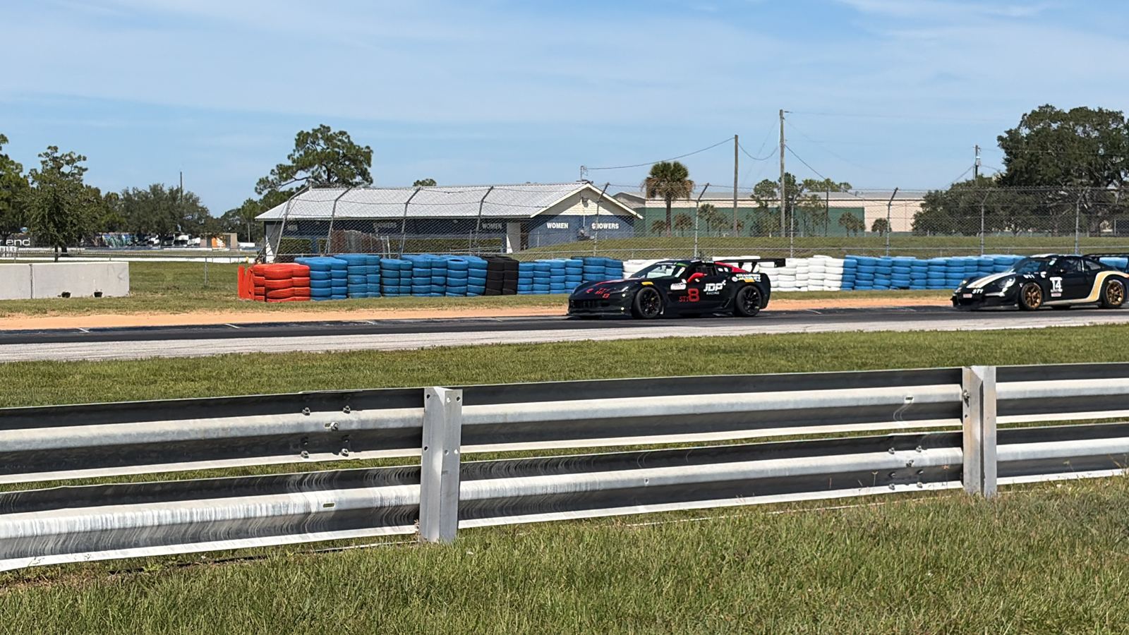 Black race car with a red rear wing passing in front of stacked tire barriers