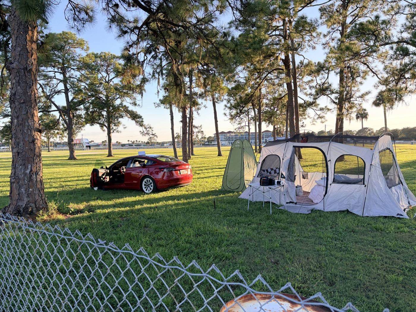 Campsite under tall pine trees at Sebring with a pop-up screen tent and a red car parked on the grass