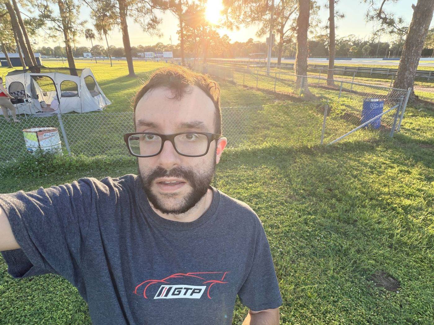 Darien smiling in a selfie at camp with the sun setting behind the trees
